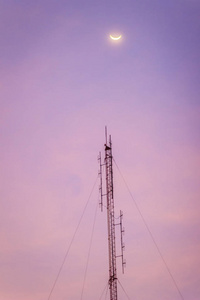 黄昏天空上的月亮和折叠的偶极子无线电天线，用于彩色天空背景的电信。 轮廓业余无线电天线塔在戏剧性的天空背景。