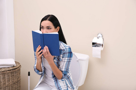 女人拿着书坐在浴室的马桶上