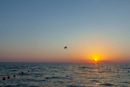 在神奇的橙色日落天空下, 动力滑翔伞在海面上翱翔飞行的剪影。滑翔伞娱乐和竞技冒险运动