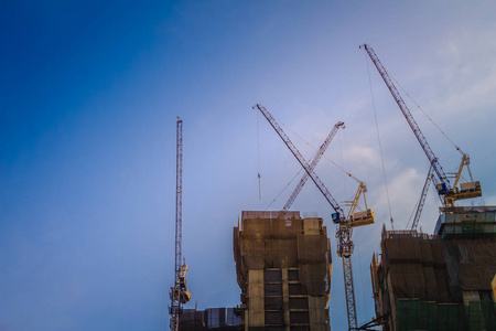 在高层建筑施工现场工程中使用吊臂塔式起重机。 摩天大楼正在建造中，塔吊在戏剧性的天空背景下。