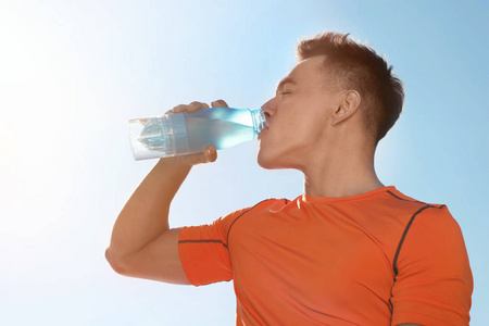 阳光明媚的一天，年轻人在蓝天的映衬下从瓶子里喝水