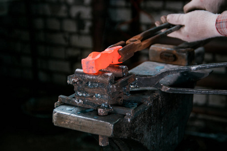 铁匠的工作区。铁匠在手套与红色热金属工件的新锤子在铁锤在锻造