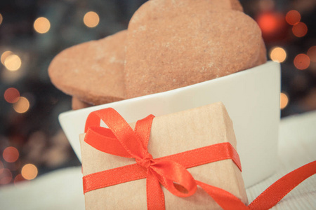 老式照片包装的礼物，带丝带的圣诞姜饼在白色的碗和圣诞树，背景灯