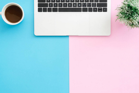 创意平面布局照片的工作空间办公桌。 顶部查看办公桌与笔记本电脑工厂和咖啡杯在蓝色粉红色背景。 顶部视图与复制空间平躺摄影。
