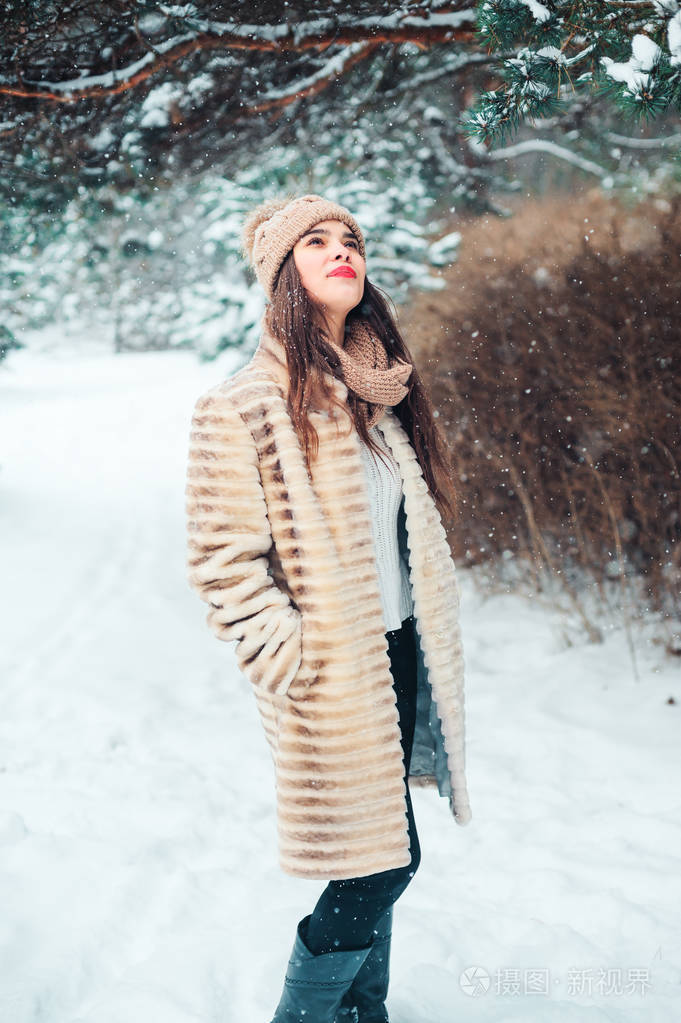 在白雪皑皑的冬林里，幸福的年轻女子在松树下散步。 季节性活动和寒假概念