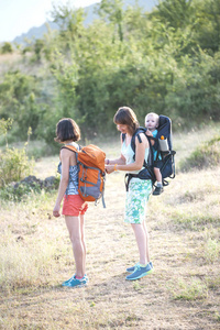 两个女人带着一个孩子旅行。 一个女人调整背包给她的朋友。 那个女孩把她儿子背在背包里。 女朋友一起旅行。 和孩子一起爬山。