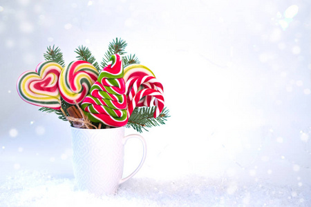 圣诞节或新年卡。 杯子上有杉树枝和彩色棒棒糖，形状为圣诞树上的雪背景。 复制空间