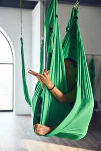 成年女性的室内拍摄在瑜伽工作室里用吊床练习不同的倒置反重力瑜伽。 身心平衡一个人的努力和成就概念