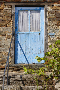 旧的生锈的蓝色木门和石屋立面。 垂直垂直垂直