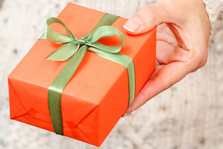 女人手里拿着一个用绿色丝带绑着的礼品盒。 浅场深选择性聚焦在盒子上。 节日或生日礼物的概念。