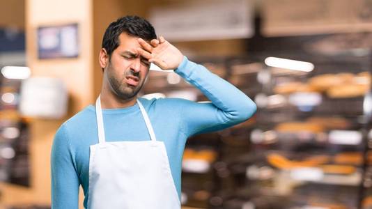 一个穿着围裙的男人，在一家面包店里，表情疲惫而病态