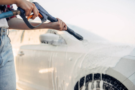 女性从车上洗掉泡沫。 年轻女子自助汽车清洗。 夏日户外车辆清洁