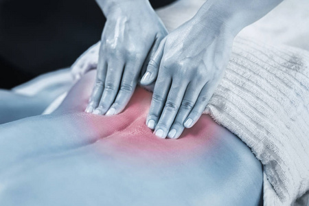关闭物理治疗师按摩女性患者受伤的下背部肌肉的图像。 蓝色的图像。 背面有红色口音。 运动损伤治疗。