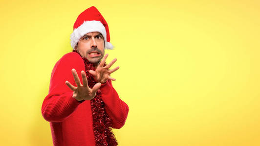 穿着红色衣服庆祝圣诞节的男人有点紧张，害怕在黄色背景下把手伸向前面