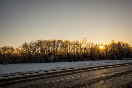 冬天的乡村道路上覆盖着冰雪，日落时有轮胎痕迹