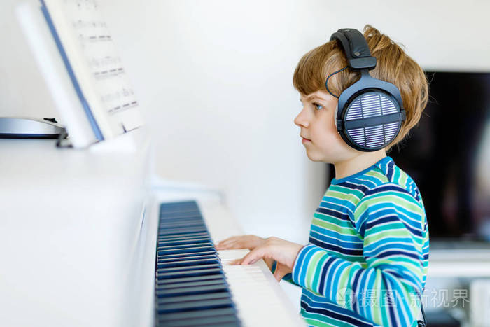漂亮的小小孩男孩戴着耳机在客厅或音乐学校钢琴.