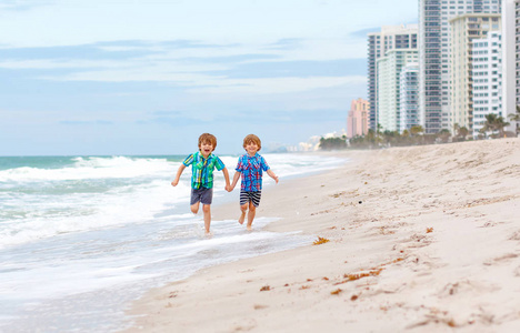 两个快乐的小孩在海边奔跑。有趣的可爱的孩子, 兄弟姐妹和最好的朋友, 在暴风雨多风的日子里度假和享受夏天。健康的孩子在迈阿密的海