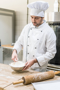 成年男性面包师在厨房的木板上撒面粉