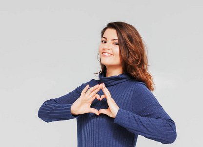 美丽浪漫的黑发女孩用双手做心脏手势,在灰色背景下微笑,与世隔绝照片