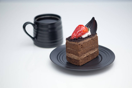 巧克力蛋糕片和草莓放在茶托里，放在白桌上的咖啡杯旁边