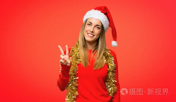 金发女人打扮成圣诞假期快乐，数着两个手指在红色背景