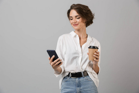 快乐的年轻商务女性的形象，在灰色的墙壁背景下，通过手机喝咖啡聊天。