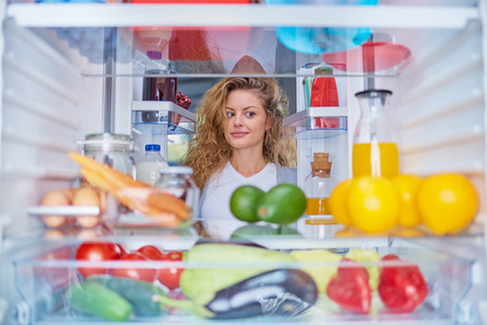 女人站在装满杂货的冰箱前，看着吃的东西。 从冰箱里拍的照片。