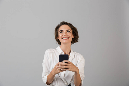 快乐的年轻商务女性的形象，在灰色的墙壁背景上，使用手机聊天，摆出孤立的姿势。