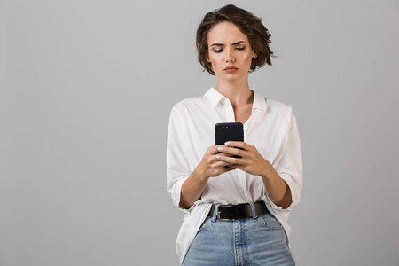 思维混乱的年轻商务女性形象，用手机聊天，在灰色的墙壁背景上摆出孤立的姿势。