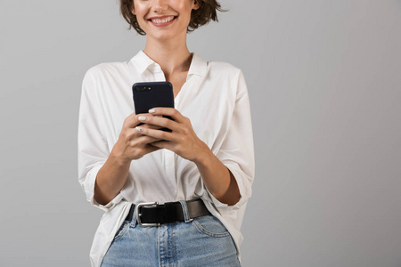 拍摄的照片，开朗的年轻商务妇女摆出孤立的灰色墙壁背景使用手机聊天。