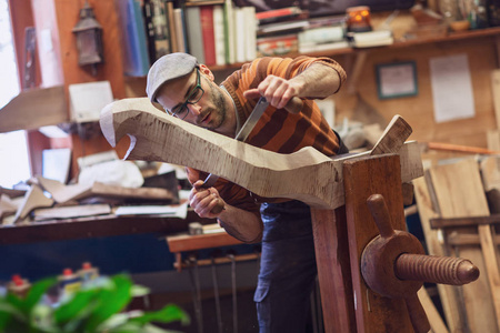 木工在车间里加工木制物品，进行测量。 半长轮廓肖像一个人穿眼镜毛衣和一个帽子模糊的背景和复制空间。