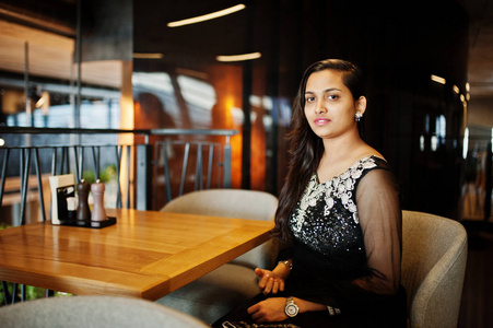 穿着黑色纱丽裙子的漂亮印度女孩在餐馆里摆好姿势。
