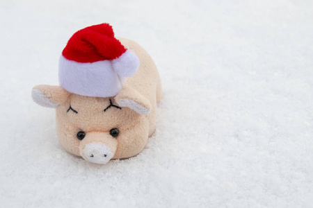 玩具粉红猪红色圣诞老人帽子在白雪上。 复制空间。 新年和圣诞节的概念。