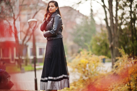 漂亮的印度女孩穿着黑色的纱丽连衣裙和皮夹克在秋街户外摆好姿势。