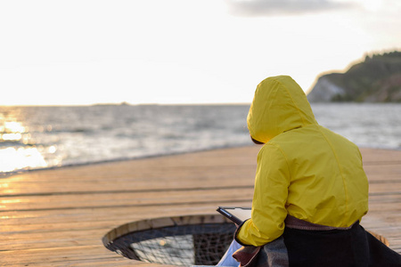 日出时穿着黄色雨衣的女人坐在码头上，拿着石碑