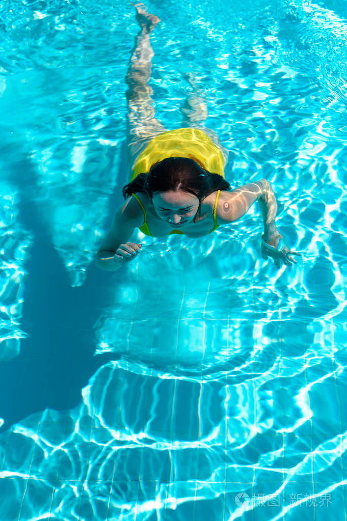 穿着黄色泳衣的女人潜入游泳池的水中,享受干净的水放松,健康