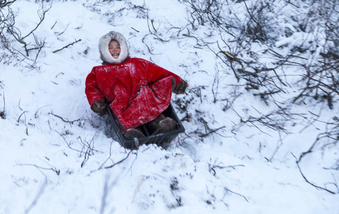 一个住在冻土带的土著居民在遥远的北方冻土带开放地区，小女孩骑在雪橇上，小女孩穿着国家红衣服。