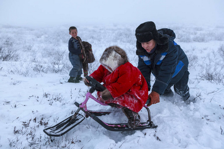 一个住在冻土带的土著居民在遥远的北方冻土带开放地区，小女孩骑在雪橇上，小女孩穿着国家红衣服。