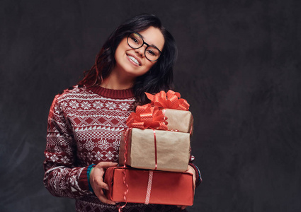 一个快乐的黑发女孩的肖像戴着眼镜和温暖的毛衣, 拿着一个礼品盒, 孤立在黑暗的纹理背景