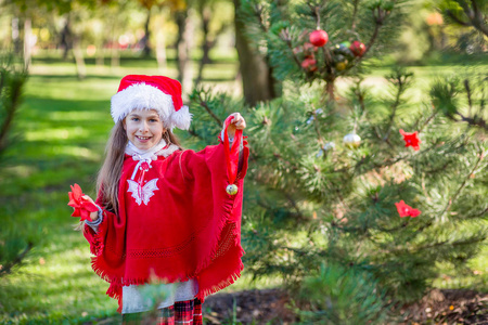 可爱的女孩在假期前在院子里户外装饰圣诞树。圣诞快乐，节日快乐。