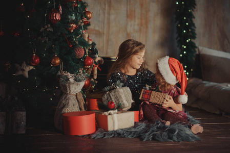 圣诞快乐，节日快乐 两个可爱的小孩子女孩姐妹在圣诞节打开魔法礼盒。 带新年装饰和圣诞树的舒适客房