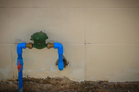 老式水表安装青铜接头PVC弯头连接器，蓝色PVC管道和红色水阀肮脏的墙壁上。