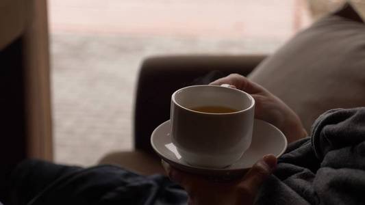 年轻女子在靠近窗户的咖啡馆喝茶, 可以看到海景。一个穿围巾和毛衣的女人喝茶, 在咖啡馆里晒太阳