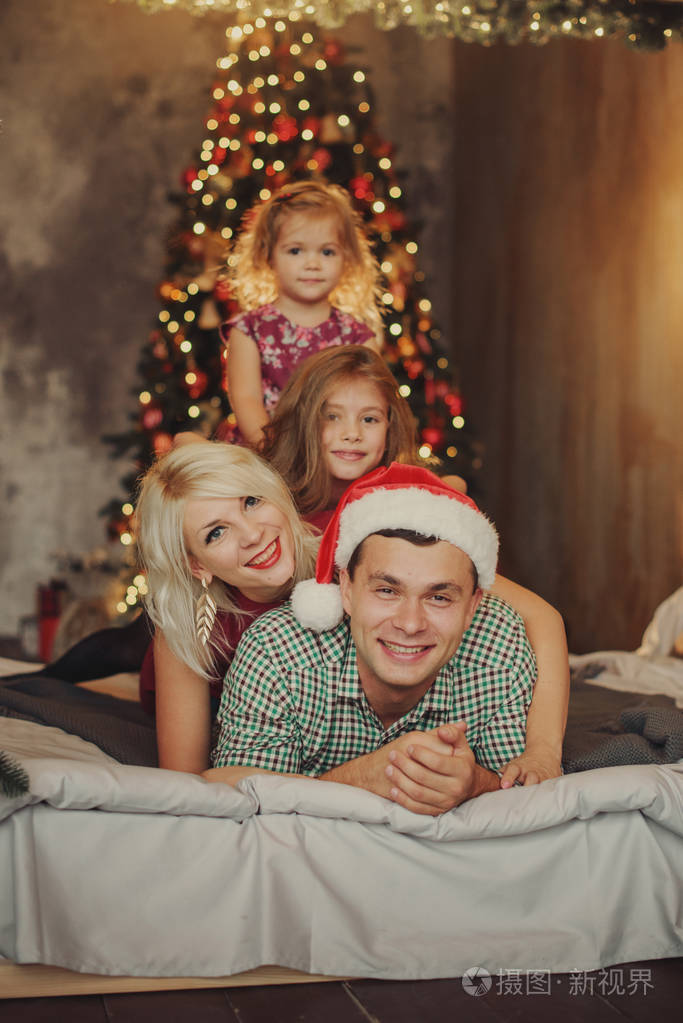 圣诞快乐节日快乐快乐的父母和两个小孩在客厅的床上一起在圣诞树附近