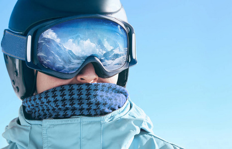靠近一个有雪山倒影的人的滑雪护目镜。 滑雪面具上反射的山脉。 滑雪场男子肖像。 戴着滑雪眼镜。 冬季运动。