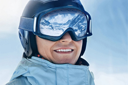 靠近一个有雪山倒影的人的滑雪护目镜。 滑雪面具上反射的山脉。 在高山和天空背景下滑雪场的人的肖像