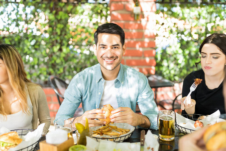 一个自信的男人拿着汉堡包，在餐馆里和女朋友一起出去玩
