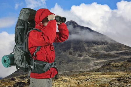 在山坡上穿着红色夹克的旅行者用望远镜观察