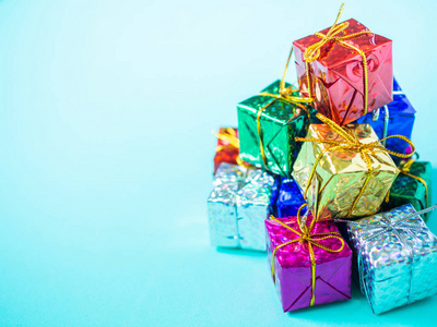 一堆五颜六色的小礼品盒在浅海蓝色背景与复制空间。 顶部的许多礼物包裹着五颜六色的闪亮的纸。