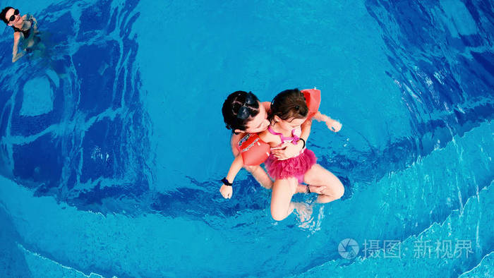 家庭母亲和女儿在豪华游泳池玩耍的鸟瞰图。 伸出舌头使滑稽的面孔微笑慢动作
